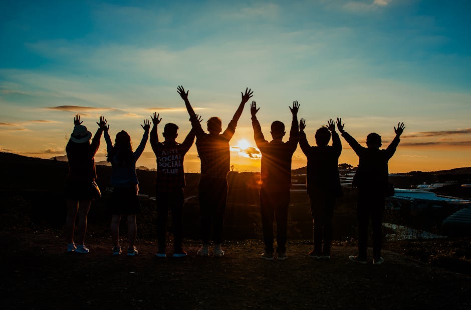 A diverse group of friends raises their arms in celebration against a vibrant sunset backdrop
